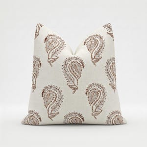 May include: A decorative pillow with a repeating paisley pattern in shades of brown and tan. The pillow has a soft, textured appearance and a neutral color palette, suitable for various home decor styles.