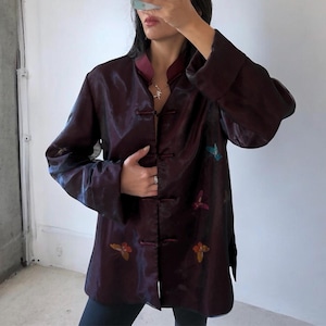 May include: A dark burgundy long-sleeved jacket featuring a mandarin collar, a front closure with fabric-covered toggle buttons, and embroidered butterfly motifs in blue, purple, and orange hues on the front panels with a smooth, shiny finish.