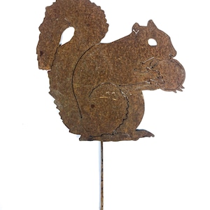 May include: A rusty brown metal squirrel garden stake. The squirrel is holding a nut and has a large, bushy tail. The stake is designed to be placed in the ground, adding a rustic touch to any outdoor space.
