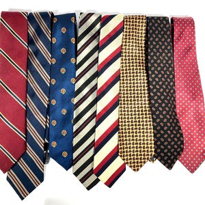 May include: A collection of seven neckties featuring various patterns including diagonal stripes in red and blue, a blue tie with small gold crests, a cream tie with red and blue stripes, a gold tie with brown paisley, and a red tie with white dots.