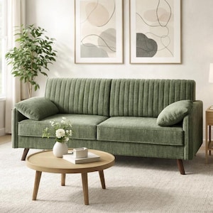 May include: A sage green sofa with vertical channel tufting, two matching throw pillows, and wooden legs. A round wooden coffee table sits in front of the sofa. Two framed abstract art prints hang on the wall above the sofa.