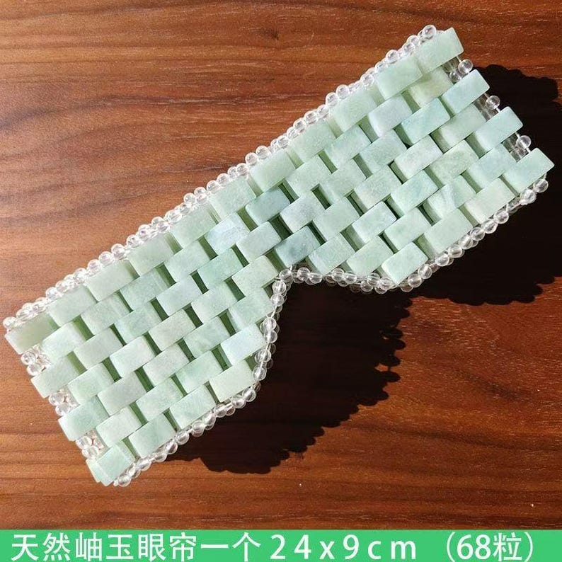 Puede incluir: Una m&aacute;scara para los ojos de jade verde claro con un patr&oacute;n de ladrillos tejidos. La m&aacute;scara mide 24 cm de largo y 9 cm de ancho, con un borde de cuentas transparentes. El texto en la parte inferior dice "M&aacute;scara de ojos de jade natural 24x9cm (68)".
