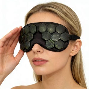 May include: Black eye mask with jade stones. The mask has a black fabric base with hexagonal jade stones. The stones are dark green and black. An elastic band secures the mask around the head.