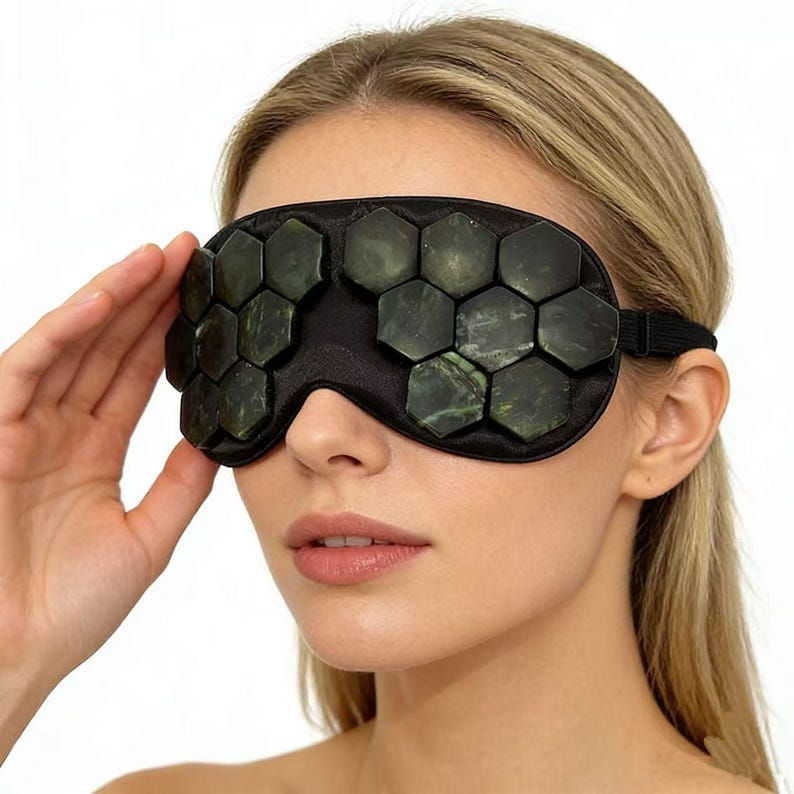 May include: Black eye mask with jade stones. The mask has a black fabric base with hexagonal jade stones. The stones are dark green and black. An elastic band secures the mask around the head.
