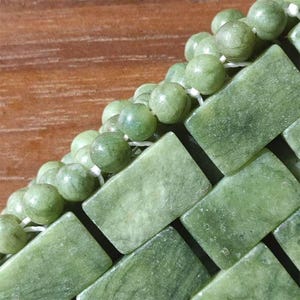 Puede incluir: Primer plano de una disposici&oacute;n de cuentas y baldosas rectangulares de piedra de jade. Las cuentas son redondas y de color verde claro, ensartadas en hilo blanco. Las baldosas son rectangulares, con un tono verde similar.