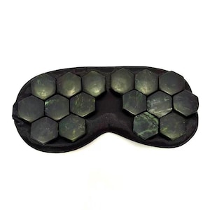 May include: A black eye mask with jade stones. The mask is black and curved to fit the face. The dark green jade stones are hexagonal in shape.