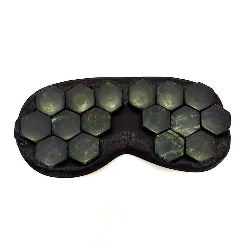 May include: A black eye mask with jade stones. The mask is black and curved to fit the face. The dark green jade stones are hexagonal in shape.