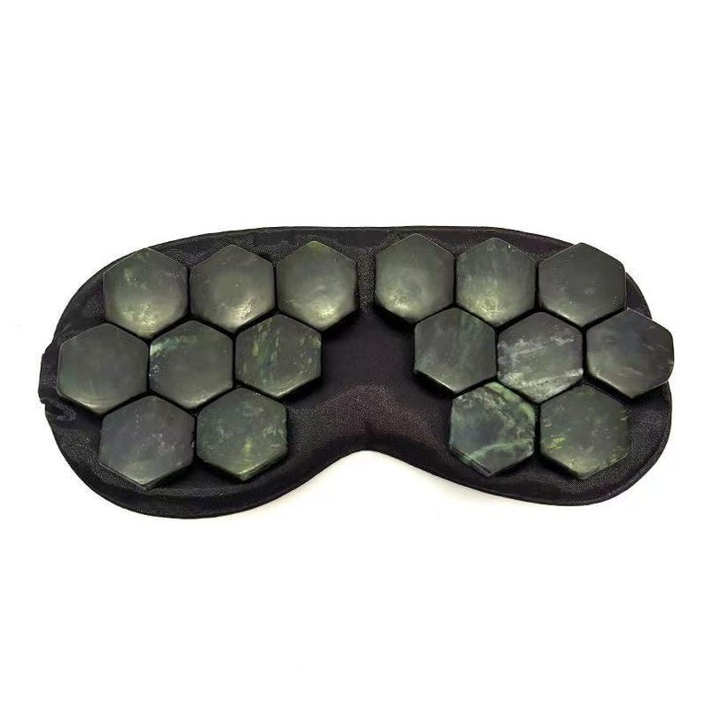 May include: A black eye mask featuring numerous dark green, hexagonal stones. The stones are arranged in two sections, covering the eye area. The mask is designed for relaxation and wellness.