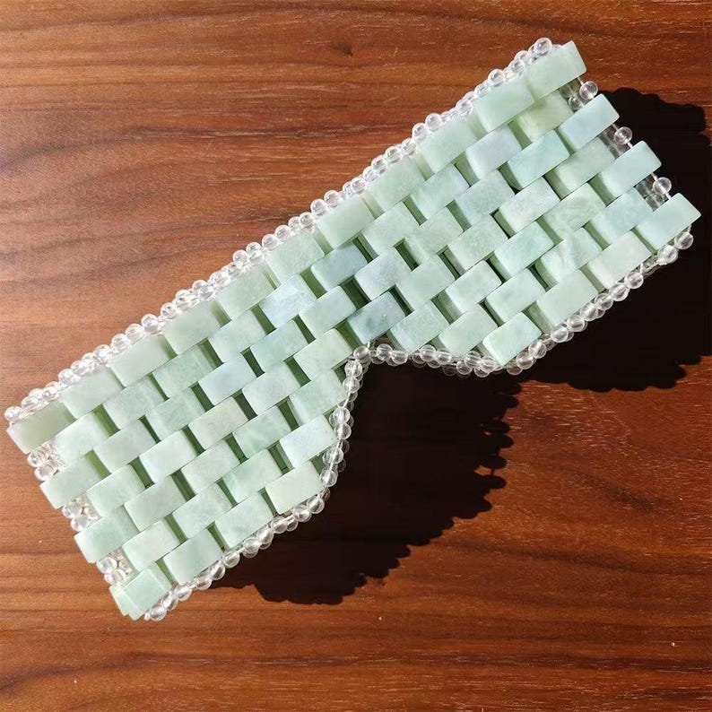 Puede incluir: Una m&aacute;scara para los ojos de jade con un dise&ntilde;o tejido. La m&aacute;scara est&aacute; hecha de peque&ntilde;as piedras rectangulares de jade en tonos verdes y blancos. Los bordes est&aacute;n bordeados con cuentas redondas y transparentes. Cubre los ojos y parte de la nariz.
