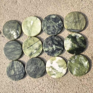 Pode incluir: Doze pedras redondas e polidas com aparência marmorizada. As pedras variam em tons de verde e cinza, com padrões de veios únicos. Estão dispostas em três fileiras de quatro sobre uma superfície castanha clara. Estas pedras podem ser usadas para fins decorativos.