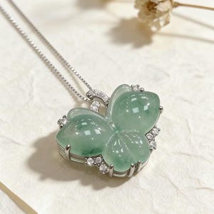Puede incluir: Un collar de plata con un colgante de mariposa. El colgante est&aacute; hecho de jade verde transl&uacute;cido, engastado en un marco de plata y adornado con peque&ntilde;as piedras preciosas claras. El dise&ntilde;o de la mariposa tiene alas redondeadas y una apariencia delicada.