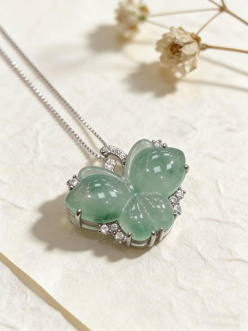 Puede incluir: Un collar de plata con un colgante de mariposa. El colgante est&aacute; hecho de jade verde transl&uacute;cido, engastado en un marco de plata y adornado con peque&ntilde;as piedras preciosas claras. El dise&ntilde;o de la mariposa tiene alas redondeadas y una apariencia delicada.