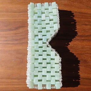 Puede incluir: Una m&aacute;scara para los ojos de color verde claro hecha de peque&ntilde;as piedras de jade rectangulares tejidas juntas. La m&aacute;scara est&aacute; bordeada con cuentas redondas y transparentes. Las piedras de jade tienen un patr&oacute;n tejido y la m&aacute;scara est&aacute; dise&ntilde;ada para cubrir los ojos.