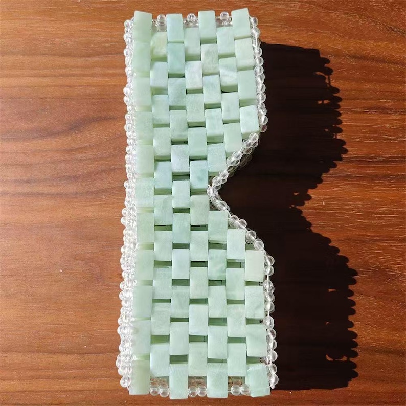 Puede incluir: Una m&aacute;scara para los ojos de color verde claro hecha de peque&ntilde;as piedras de jade rectangulares tejidas juntas. La m&aacute;scara est&aacute; bordeada con cuentas redondas y transparentes. Las piedras de jade tienen un patr&oacute;n tejido y la m&aacute;scara est&aacute; dise&ntilde;ada para cubrir los ojos.