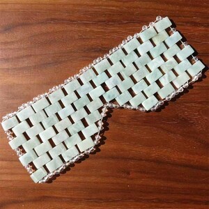 Puede incluir: Una m&aacute;scara de ojos de jade con un dise&ntilde;o tejido. La m&aacute;scara est&aacute; hecha de piedras de jade rectangulares de color verde claro, conectadas por una cadena de cuentas transparentes. La m&aacute;scara est&aacute; dise&ntilde;ada para cubrir los ojos y parte de la cara.