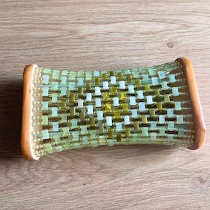 May include: A rectangular massage pillow featuring a curved wooden frame on both ends. The centre consists of a grid of small, light green and olive green rectangular beads strung together with clear wire, creating a flexible, woven surface structure.