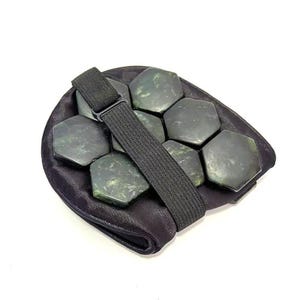 May include: A black jade stone massage tool with a black elastic strap. The tool features multiple hexagonal jade stones set in a black fabric pouch. The stones are a dark green colour.