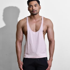 Puede incluir: Una camiseta sin mangas rosa claro con cuello redondo. La camiseta sin mangas se combina con pantalones deportivos negros. La imagen se toma frente a un fondo blanco.