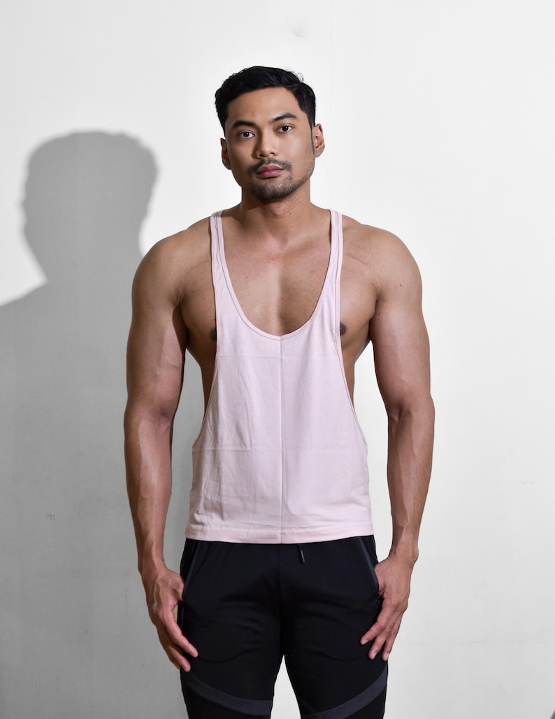 Puede incluir: Una camiseta sin mangas rosa claro con cuello redondo. La camiseta sin mangas se combina con pantalones deportivos negros. La imagen se toma frente a un fondo blanco.