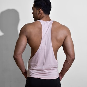 Puede incluir: Camiseta sin mangas rosa claro con dise&ntilde;o de espalda deportiva. La camiseta sin mangas se combina con pantalones deportivos negros. La persona est&aacute; de espaldas, con las manos en los bolsillos, sobre un fondo blanco.