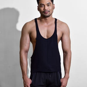 Puede incluir: Una camiseta sin mangas negra con cuello en U profundo y tirantes anchos. La camiseta sin mangas se combina con pantalones cortos deportivos negros. La persona est&aacute; de pie frente a un fondo blanco.