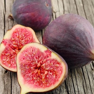 May include: Close-up of fresh figs, some whole and some sliced open. The figs are a deep purple color with a vibrant red interior. The image is taken on a rustic wooden surface.
