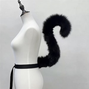 May include: A black faux fur tail attached to a mannequin with a black belt. The tail is long and fluffy, curving upwards. The mannequin is white, and the background is a plain white.