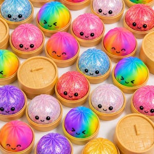 May include: A collection of colorful, smiling, glittery dumpling-shaped toys in small, tan, lidded containers. The dumplings are various colors, including blue, pink, purple, yellow, and rainbow, with smiling faces. The containers are arranged on a white surface.