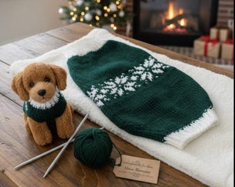 May include: A brown plush dog wearing a green and white snowflake-patterned sweater sits next to a matching sweater. A ball of green yarn, knitting needles, and a tag are also on the wooden table. A Christmas tree and fireplace are in the background.
