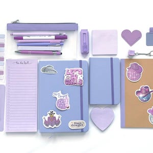 May include: An assortment of purple stationery, including notebooks, pens, sticky notes, and a pencil case. The notebooks feature stickers with the text "Let's Go Girls" and "Disco Cowgirl". A bookmark with a tassel is also included.