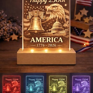 May include: A lighted acrylic sign with the text "Happy 250th" and "America 1776-2026". The design features an eagle, the Liberty Bell, and the Capitol building. The sign sits on a wooden base and is illuminated with LED lights.