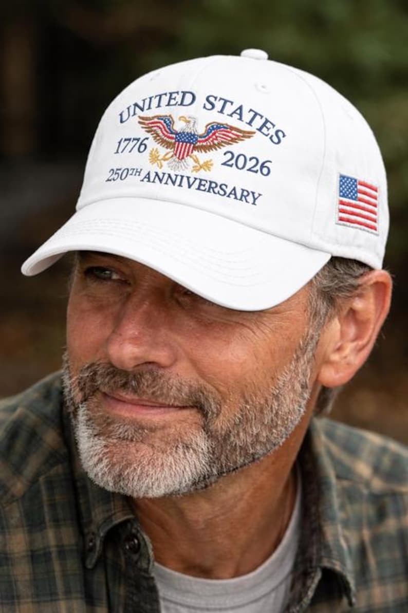 Puede incluir: Gorra de b&eacute;isbol blanca con el texto "UNITED STATES 1776 2026 250TH ANNIVERSARY" y un &aacute;guila. La gorra tambi&eacute;n presenta una peque&ntilde;a bandera estadounidense en el lateral. Un accesorio patri&oacute;tico cl&aacute;sico.
