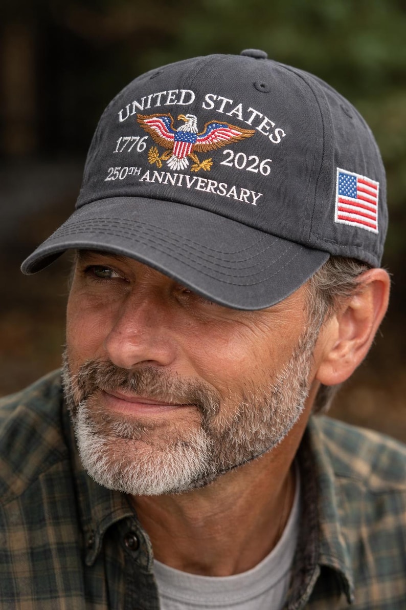 Puede incluir: Gorra de b&eacute;isbol gris oscuro con texto bordado en blanco "UNITED STATES 1776 2026 250TH ANNIVERSARY". La gorra presenta un dise&ntilde;o de &aacute;guila bordada y una peque&ntilde;a bandera americana en el lateral.
