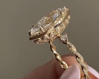 May include: A gold ring featuring a large marquise-cut center stone surrounded by a halo of smaller round stones. The setting includes intricate circular metalwork details, and the band has a twisted design encrusted with tiny pavé diamonds.