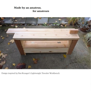 May include: A wooden workbench with a light brown tabletop and a lower shelf, set against a gray stone surface. The text "THE LEARNER'S WORKBENCH" is at the top. The design is inspired by Rex Krueger's Lightweight Traveler Workbench.