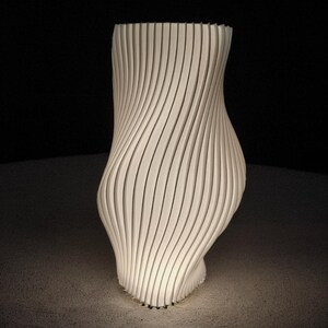 May include: A white, abstract sculpture with a distinctive, curved design. It's made of vertical, parallel lines that twist and turn, creating a dynamic form. The sculpture is lit from below, highlighting its texture. The piece is a modern art object.