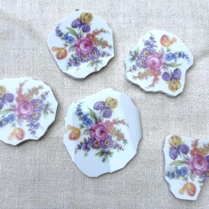 May include: Five irregular white ceramic shards featuring a colorful floral pattern. Each piece displays a central pink rose surrounded by smaller blue, purple, orange, and yellow flowers with green leaves, creating a consistent botanical design.