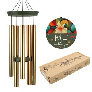 May include: A wind chime with gold-colored tubes and a dark green top and clapper. A circular decoration with a floral design and the text "Mom, we love you" hangs nearby. A brown box with the brand name is also visible.
