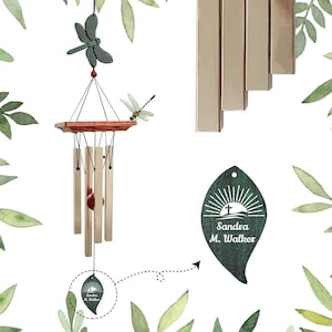 May include: A wind chime with a wooden top and metal chimes. The wind chime is decorated with a green dragonfly and a leaf-shaped tag with the text "Sandra M. Walker". The chimes are a light gold color.