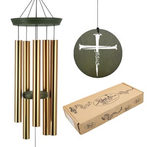 May include: A wind chime with gold-colored tubes and a dark green top and clapper. A round, dark green disc with a white cross and the word "Jesus" is hanging from the top. A brown box with the brand name is in the image.