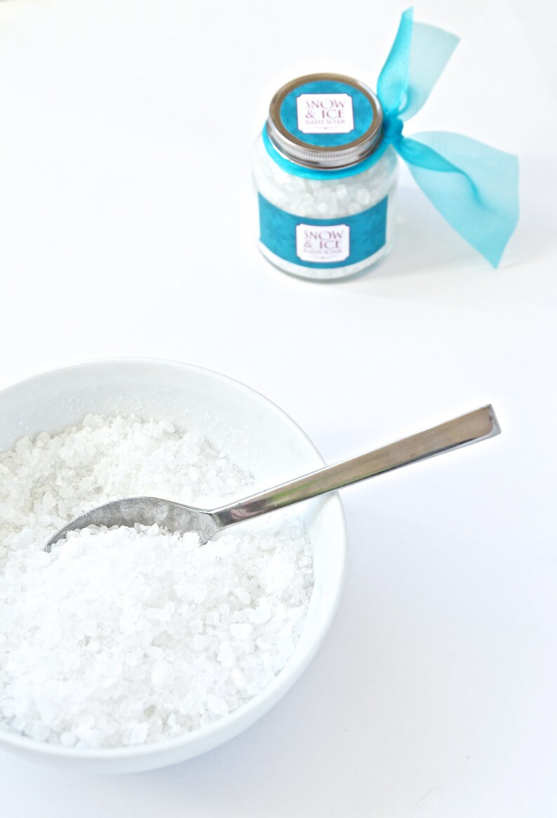 May include: A white ceramic bowl filled with coarse, white salt and a silver spoon. A glass jar with a silver lid and a teal label reading "Snow & Ice Bath Soak" is tied with a teal ribbon. The jar is also filled with white salt.