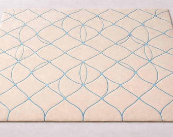Può includere: Un tappeto rettangolare beige con un motivo geometrico ripetuto in azzurro. Il design presenta forme a diamante interconnesse con linee curve e piccoli accenti circolari, creando un'estetica moderna.