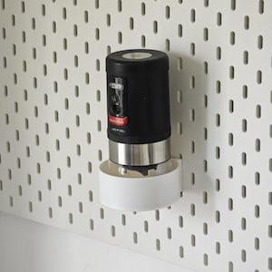 以下が含まれることがあります： 白のペグボードに取り付けられた、黒とシルバーのキッチン家電。白いベースが付いています。家電には赤いアクセントと「oceanrich」の文字があります。ペグボードには、等間隔に配置された楕円形の穴があります。