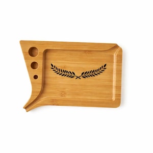 May include: A bamboo tray with a unique shape, featuring a rectangular area and a curved edge with three circular cutouts. A black laurel wreath design is centered on the tray. The tray is made of light brown bamboo.