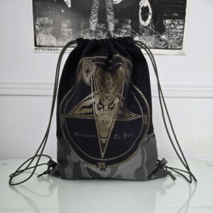 Könnte beinhalten: Schwarzer Kordelzugrucksack mit einem goldenen Pentagramm und Ziegenkopf-Design. Der Text "Welcome To Hell" ist unter dem Bild aufgedruckt. Der Boden der Tasche ist Camouflage.