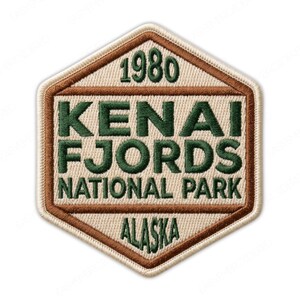 May include: Embroidered patch with a hexagonal shape. The patch features the text "KENAI FJORDS NATIONAL PARK ALASKA 1980" in green and brown stitching on a beige background. The border is brown.