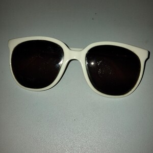 May include: White sunglasses with dark lenses. The sunglasses have a rounded, square shape.