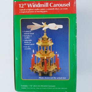 May include: A rectangular green box for a 12" Windmill Carousel. The packaging features a graphic of a multi-tiered wooden carousel with six red candles, a windmill top, and text including "JoyBrite" and "12" Windmill Carousel" with product details.