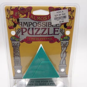 May include: A teal four-piece pyramid puzzle packaged in a clear plastic blister pack. The yellow backing card features illustrations of jesters and columns with the text Nearly Almost Impossible Puzzle 4 Piece Pyramid and Fit the four pieces together to make a pyramid.