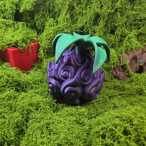 Puede incluir: Una fruta morada estilizada con hojas verdes, sobre un fondo de musgo verde. La fruta tiene un diseño arremolinado y texturizado. Una forma geométrica roja es parcialmente visible en el fondo, agregando un toque de color.